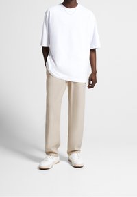 White oversized t-shirt with a round neck, paired with beige wide-leg trousers and white sneakers with gum soles. Simple, clean design.