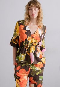 Top peplum floral de culoare maro închis, cu flori portocalii, roz și verzi; mâneci scurte și decolteu în V. Pantaloni florali asortați completează ținuta.
