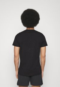 Czarna bawełniana koszulka z krótkim rękawem, z okrągłym dekoltem, dopasowany krój, gładka faktura, bez widocznych wzorów ani grafik, noszona w połączeniu z ciemnymi szortami.