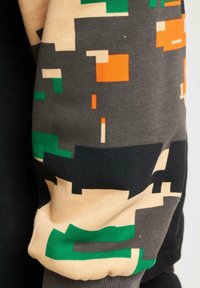 Long-sleeve garment with a color-blocked design. Main colors: black, beige, green, orange, and gray. Patterns include geometric shapes and textures.