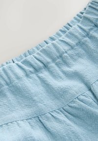 Világoskék anyag, melynek texturált halászmintázata van, és behúzható rugalmas derékpánttal rendelkezik; a designja könnyed, redőzött.