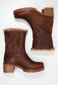 Botas de cuero marrón con un acabado texturizado, parte superior forrada de piel de huevo y un tacón de madera grueso. Suela de goma con dibujo para mayor tracción.