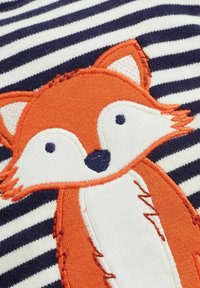 Gestreifter Stoff in Marineblau und Weiß zeigt einen orangefarbenen gestickten Fuchs mit weißen Akzenten und schwarzen Augen, der Textur und Detail hervorhebt.