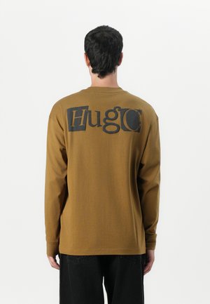 Long-sleeve brown shirt featuring a large black "Hugo" logo on the back. Made of cotton with a smooth texture and regular fit.