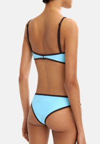 Niebieski kostium kąpielowy składający się z jasnoniebieskiego materiału z brązowym wykończeniem, regulowanymi ramiączkami i zapięciem na plecach. Gładka faktura.