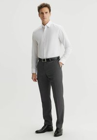 Biała koszula z długim rękawem, połączona z ciemnoszarymi spodniami w kratę i czarnymi skórzanymi butami. Pasek ma błyszczącą klamrę.