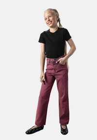 Czarny prążkowany t-shirt z krótkim rękawem, różowe dżinsowe szerokie spodnie z wysokim stanem i czarne baleriny z okrągłymi wycięciami. Stoi z jedną ręką na biodrze.