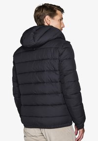 Sort pufferjakke med hætte, der har quiltede sektioner, en glat overflade og et tætsiddende design til varme. Inklusive trykknaplukninger ved ærmerne.