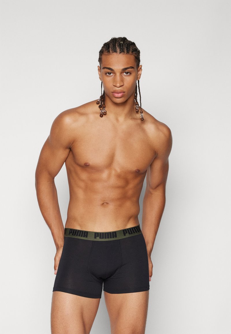 Boxer briefs pretos com uma faixa verde com o logótipo "PUMA". Tecido suave e design ajustado; modelo exibe o produto.