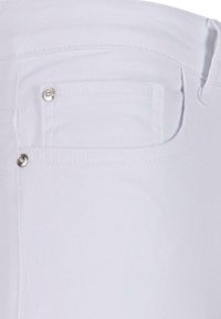 Jeans din denim alb cu un buzunar pe spate dotat cu elemente metalice argintii și o textură netedă. Cusăturile sunt vizibile pe alocuri.