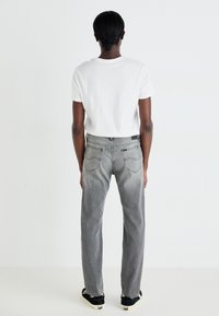 Jean gris avec une coupe droite, poches arrière et dégradé subtil, associé à un t-shirt blanc ajusté et des baskets noires.