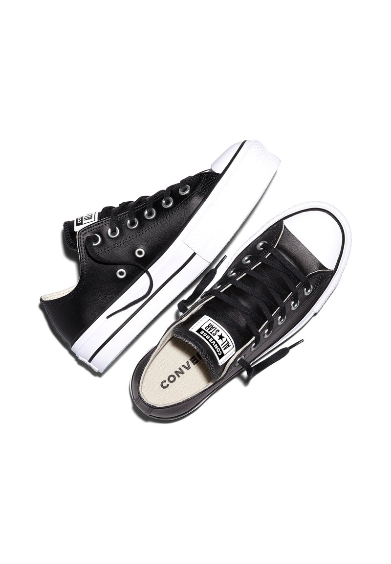Paar schwarze niedrige Converse All Star Sneaker mit weißen Gummisohlen und schwarzen Schnürsenkeln vor weißem Hintergrund.