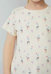 Lichtgele geribbelde t-shirt met een kleurrijke print van kleine figuren, palmbomen en fruitmotieven. Korte mouwen en een ronde halslijn.