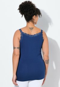 Donkerblauwe tanktop met kantafwerking langs de halslijn en schouderbanden, gemaakt van een gladde, elastische stof, aansluitende stijl, gezien vanaf de achterkant.