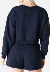 Felpa corta blu navy scura con maniche lunghe e vestibilità rilassata, abbinata a pantaloni corti coordinati. Tessuto morbido con dettagli di cucitura minimi.