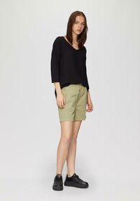 Zwarte, loszittende V-hals top met 3/4 mouwen, gecombineerd met lichtgroene knielange shorts en zwarte sneakers met dikke zolen.
