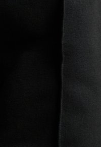 Svart tyg med en texturerad stickning, med släta områden och små variationer i tjocklek, vilket skapar ett lagerutseende.