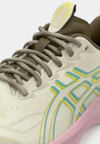 Μπεζ αθλητικό παπούτσι με υφασμάτινη επιφάνεια, με τιρκουάζ και κίτρινες λεπτομέρειες, καφέ κορδόνια και ροζ ενδιάμεση σόλα. Κατασκευασμένο από ελαφρύ, αναπνεύσιμο υλικό.