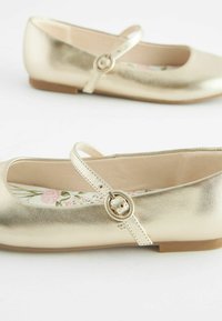 Ballerine metalliche oro con punta arrotondata e una striscia singola dotata di fibbia circolare. Soletta con motivo floreale e suola piatta.