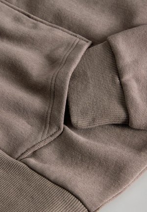 Brown cotton fabric of a hoodie, featuring ribbed cuffs and hem, with a soft texture and visible stitching details.