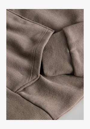 Hnedá bavlnená látka mikiny, s rebrovanými manžetami a lemom, s jemnou textúrou a viditeľnými švami.