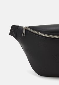 Crna kožna torba s teksturiranom površinom, ugraviranim logotipom, srebrnim zatvaranjem na rajsferšlus i trokutastim detaljem s jedne strane.