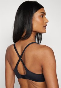 Black bra featuring a smooth, matte finish, adjustable crisscross straps, and a hook-and-eye closure at the back for support and fit.