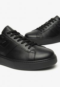 Sneakers in pelle nera con una finitura liscia, punta rotonda e suola in gomma testurizzata. I lacci sono neri, con un branding minimale sul lato.