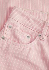 Ružičasta prugasta traper tkanina ima prednji džep s bijelim šavovima i srebrnim hardverom. Tekstura je glatka s blagim sjajem.