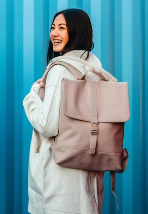 Light pink backpack with a fold-over flap, adjustable straps, and a buckle closure. Made from smooth material, featuring a simple design.