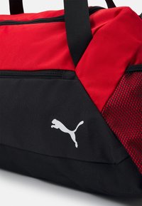 Rode en zwarte sporttas gemaakt van gestructureerde stof. Bevat een wit Puma-logo en een mesh-paneel, met stevige zwarte handvatten.