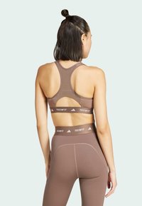 Sujetador atlético marrón con diseño de espalda nadadora y corte, combinado con leggings de alta cintura a juego que cuentan con una banda con logo y detalles de costura.