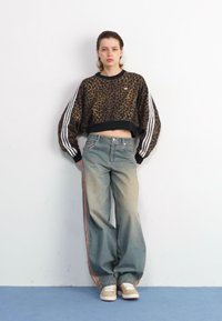 Cropped Sweatshirt mit Leopardenmuster und schwarzem Rippstrick, kombiniert mit hellblauen, weit geschnittenen Jeans mit seitlichen Streifen. Tanfarbene Sneakers runden den Look ab.