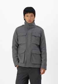 Chaqueta de mezcla de lana gris con cuello alto, que cuenta con cuatro bolsillos de solapa y hombreras. Diseñada para una silueta ajustada.