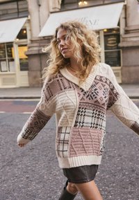 Knit sweater featuring a mix of patterns in beige, pink, and brown, with a V-neck and ribbed cuffs, offering a textured appearance.