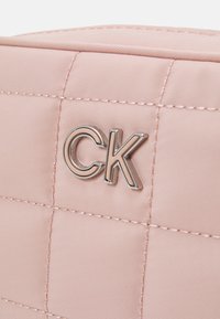 Růžová prošívaná kabelka s jemným stříbrným logem "CK". Vnější strana má hladký povrch s prošívanými liniemi a pevnou strukturu.