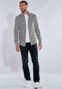 Herrenhemd in strukturiertem Grau mit Kragen, kombiniert mit schwarzen Jeans und weißen Sneakers. Das Hemd hat sichtbare Druckknöpfe.