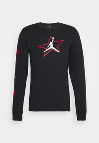 T-shirt noir à manches longues en coton avec un logo Jordan blanc à l'intérieur d'une étoile rouge sur la poitrine et du texte rouge sur la manche gauche.