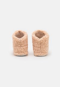 Chaussons en peluche de couleur pêche avec une texture moelleuse, une ouverture arrondie et une semelle blanche, conçus pour le confort et la chaleur.