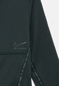 Tumši zaļš audums ar Nike logo un frāzi "NAV BEIGU LĪNIJAS", kas izdrukāta netālu no kabatas un šuves.