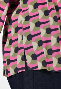 Blusa colorata con un motivo geometrico nei colori rosa, verde oliva, beige e blu navy. Ha un orlo arrotondato con spacchi laterali.
