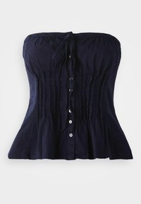 Αμάνικο τοπ σε στυλ κορσέ ναυτικού μπλε χρώματος με κάθετες πιέτες, μπροστινά κουμπιά και δεμένο φιόγκο στον λαιμό, σε άσπρο φόντο.