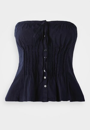 Haut sans bretelles de style corset bleu marine avec des plis verticaux, boutons à l'avant et un nœud attaché au niveau du col sur fond blanc.