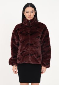 Burgundyröd fuskpälsjacka med hög krage, dragkedjestängning och svarta vågmönster. Har lös passform och voluminösa ärmar.