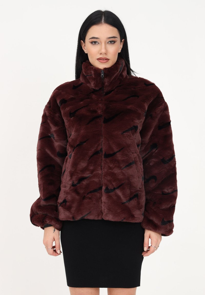 Veste en fausse fourrure bordeaux avec col haut, fermeture éclair et motifs en vagues noires. Présente une coupe ample et des manches volumineuses.