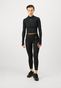 Czarny krótki top z długim rękawem oraz legginsy z wysokim stanem, zdobione prążkowanymi akcentami. Oba elementy mają małe białe logo Nike. Czarne buty sportowe dopełniają stylizację.