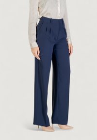 Pantalons plissés marine avec une coupe ajustée, en tissu lisse. Présentent une taille haute et des jambes larges. Associés à un chemisier léger à motifs.