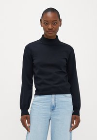 Melnas turtlenecka formas džemperis ar garām piedurknēm, ar ribotām aprocēm un apakšmalu. Valkā ar gaiši ziliem augstu jostasvietu džinsiem. Gluda tekstūra.