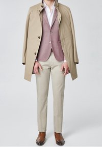 Trench coat beige sopra un gilet rosa chiaro, camicia bianca e pantaloni beige. Scarpe in pelle marrone. Stile formale con una vestibilità su misura.