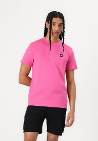 Lyserød bomulds-t-shirt med korte ærmer, rund halsudskæring og et lille sort mærke på venstre side, parret med sorte cargo-shorts.
